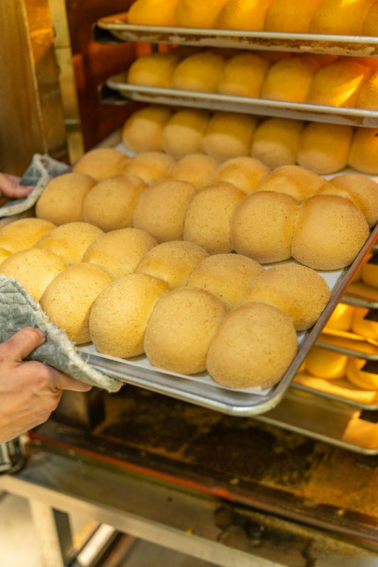 A person holding a tray of bread in front of a rack of bread rolls
